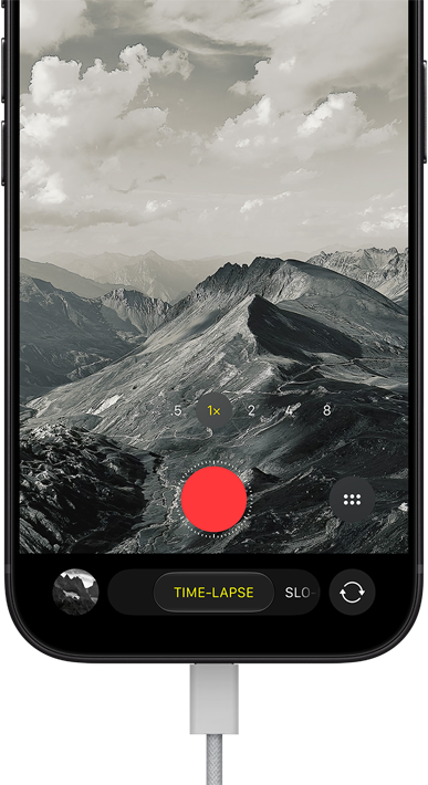 iPhone 18 Pro, front exterior, displaying a mountainous landscape, with the camera mode overlay in Time-Lapse mode, with charging cable attached to charging port