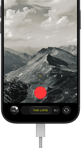 iPhone 18 Pro, front exterior, displaying a mountainous landscape, with the camera mode overlay in Time-Lapse mode, with charging cable attached to charging port