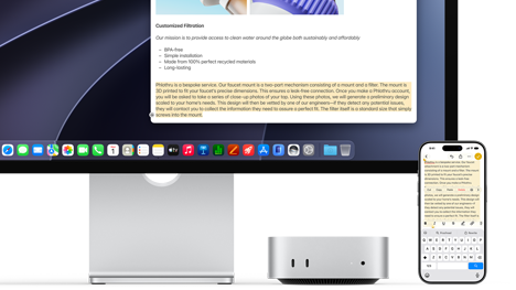 Mac mini front, tucked under Studio Display, an iPhone sits to the right of the device and the display, text selected with cut, copy, paste and AutoFill commands above on iPhone matches highlighted text on display, showcasing Universal Clipboard