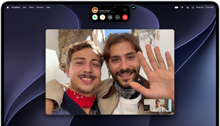 MacBook Pro with PROLED XDR Display, silver colour, display shows a video call in progress with two people in a sunlit town waving to a person at home