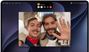 MacBook Pro with PROLED XDR Display, silver colour, display shows a video call in progress with two people in a sunlit town waving to a person at home